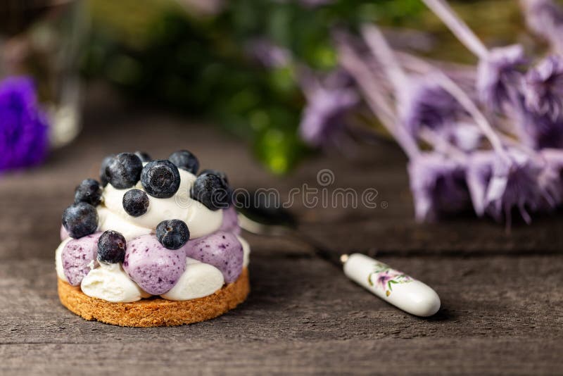 White chocolate and blueberry sable tartelette with vintage spoon on a dark grey wood table over a purple dry flowers background stock photos White chocolate and blueberry sable tartelette with vintage spoon on a dark grey wood table over a purple dry flowers background stock photos