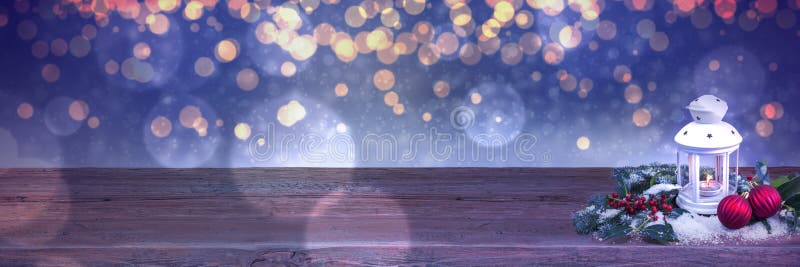 White Christmas Lantern on a wooden table in front of a dark blue blurred lights background.
