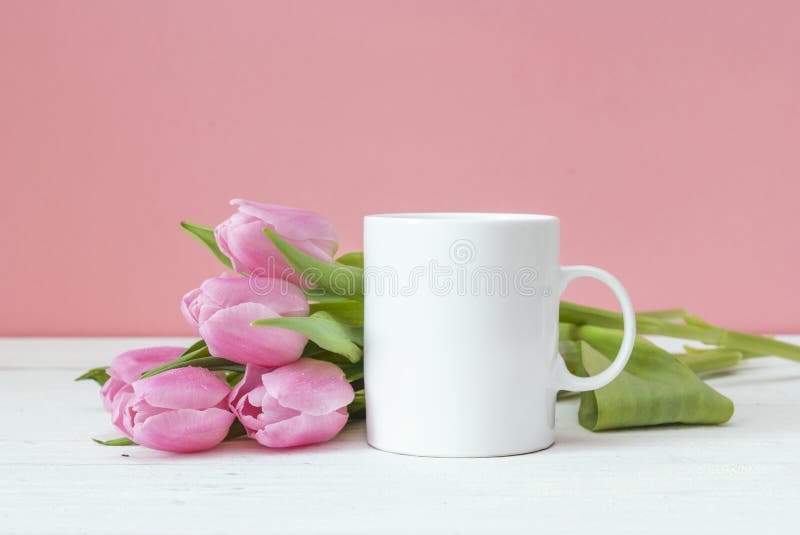 White coffee mug with pink tulips on a pink background. Space for text or design.