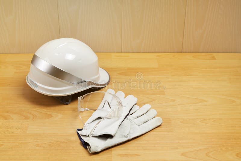 White Construction Helmet, Safety Goggles and Leather Gloves on Table