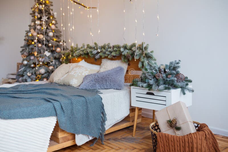 White cozy modern bedroom with holiday decoration. Wooden bed in scandinavian style room with festive Christmas tree in