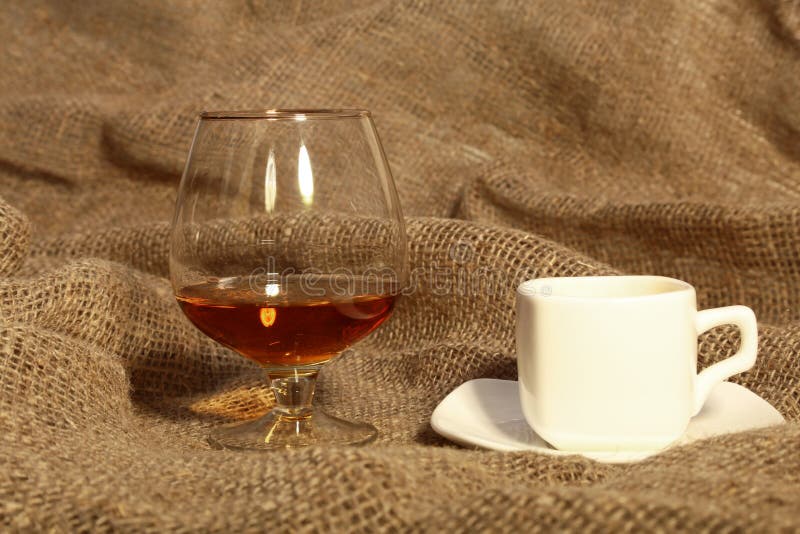 White Cup of Coffee and Cognac or Brandy in a Glasses on Old Textile