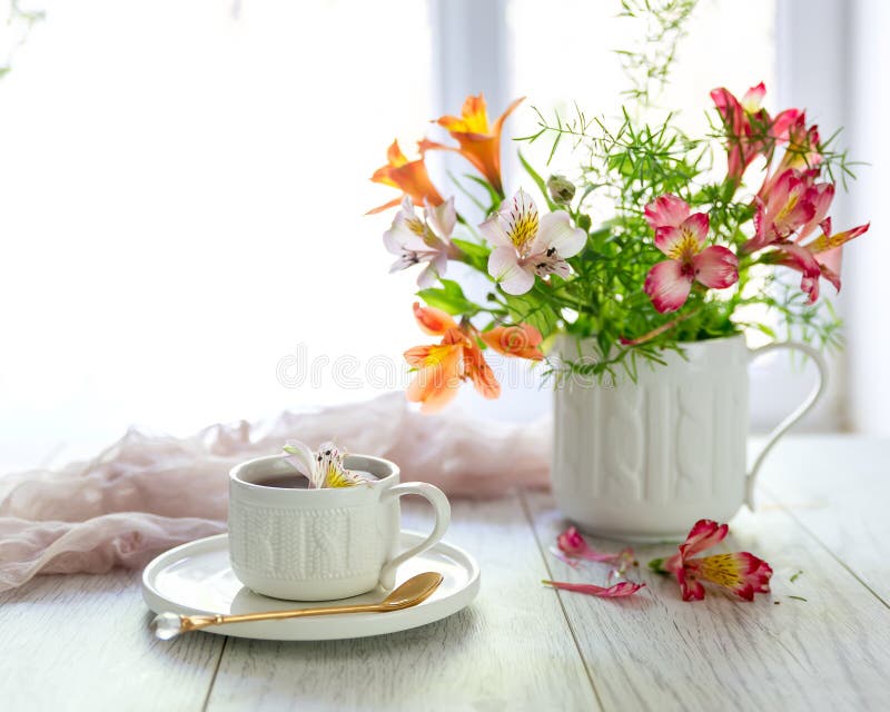 White cup with tea on the table. Flowers nearby