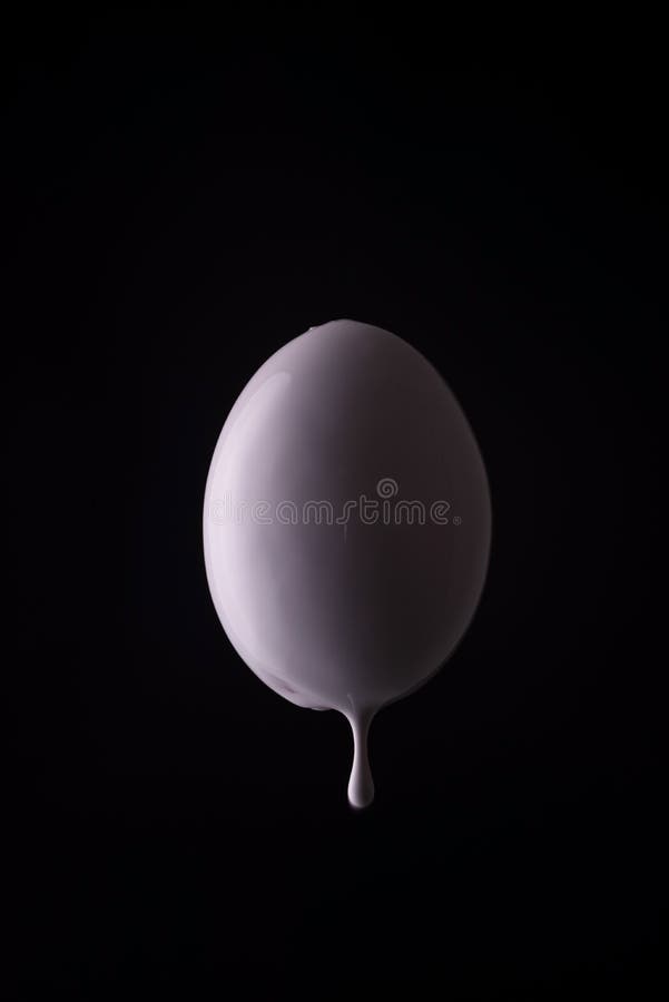 White Egg Dripping with Drops of White Paint on a Black Background