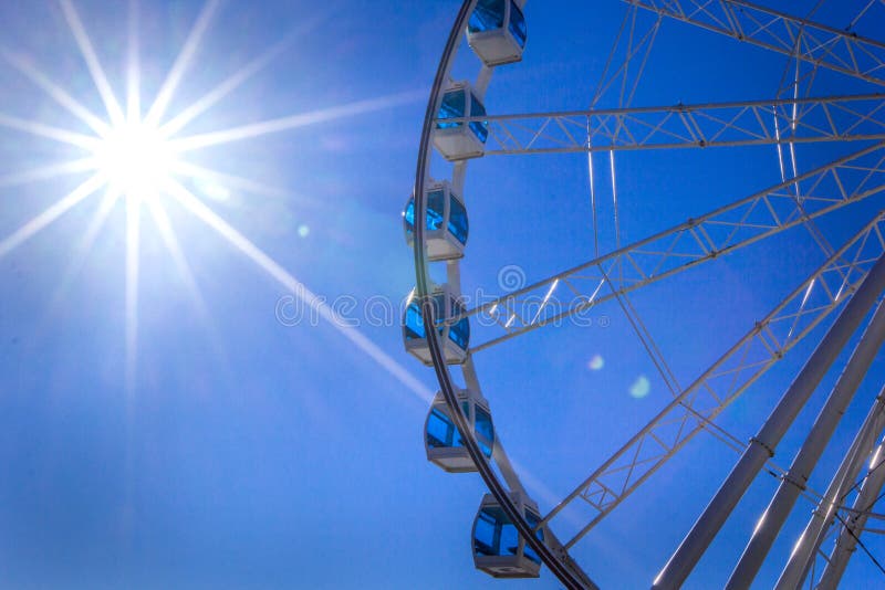 White Ferris wheel with glass light-blue booths against the blue sky and summer sun with bright rays, Helsinki, Finland