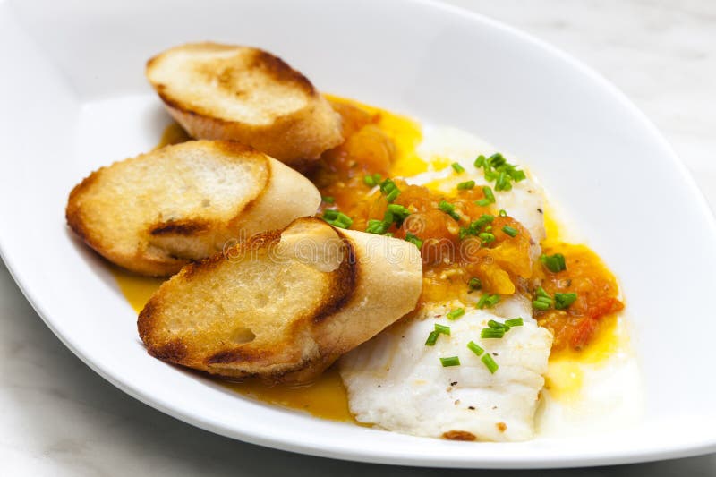 White Fish with Tomato Sauce and Roasted Baguette Slices Stock Photo