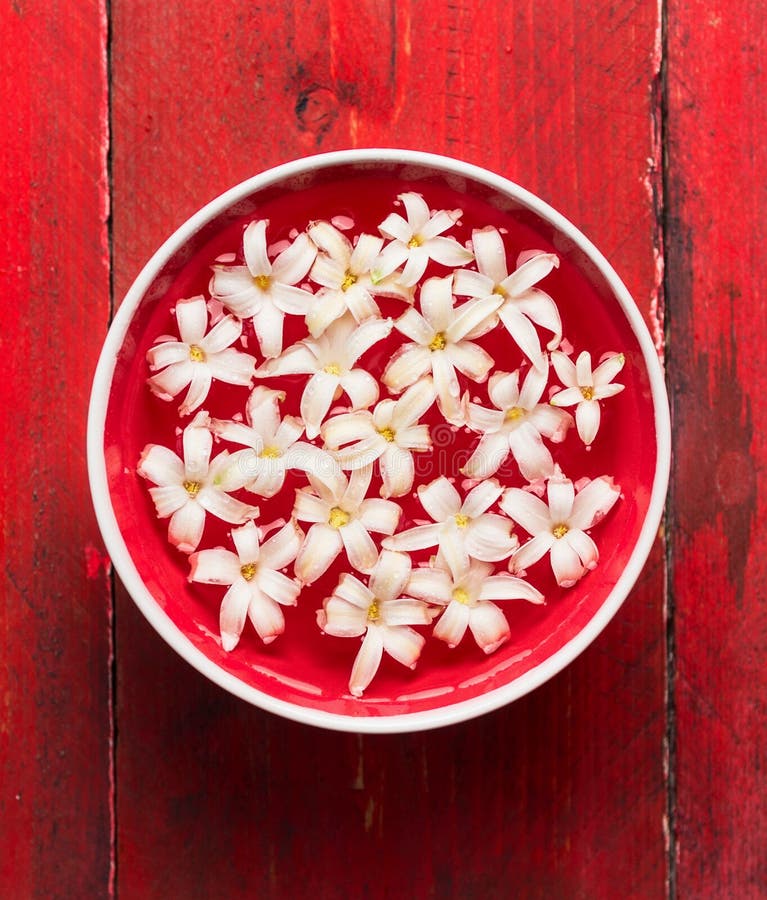 White flowers in Bowl with water on red wooden table, SPA background