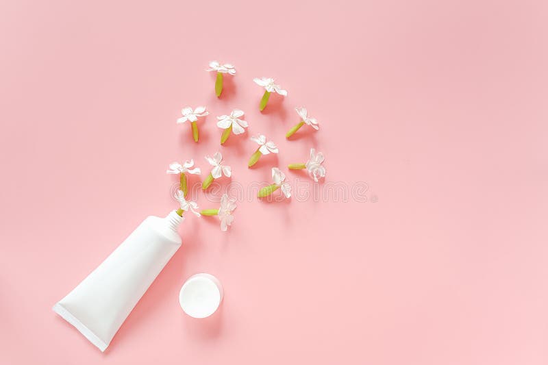 White flowers and cosmetic, medical white tube for cream, ointment, toothpaste or other product on pink background. Concept