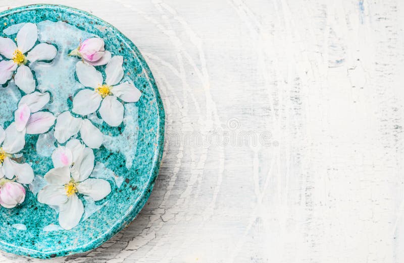 White flowers in turquoise blue water bowl on light shabby chic wooden background, top view, place for text. Wellness and spa