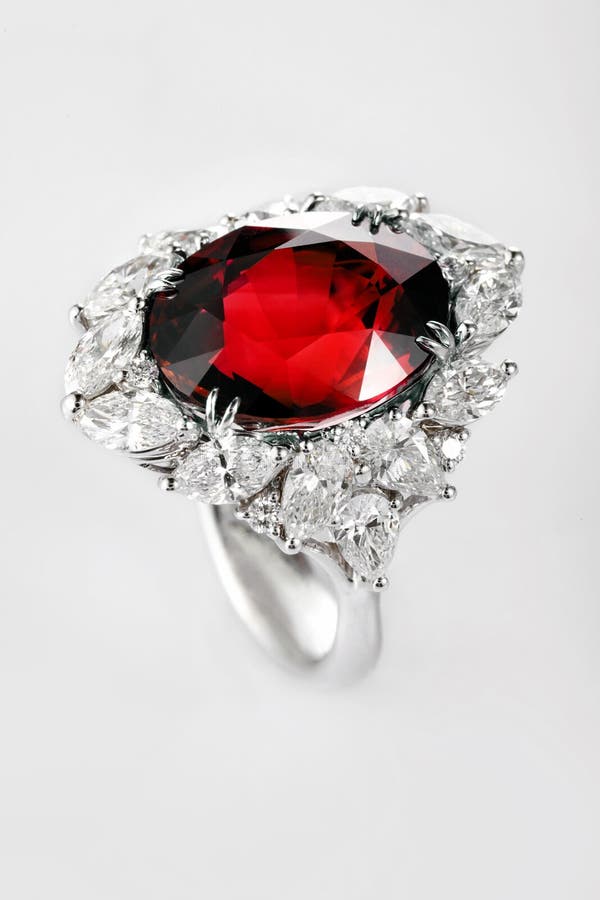 White gold or silver ring with diamonds and red ruby gemstone on gray background. Selective focus. White gold or silver ring with diamonds and red ruby gemstone on gray background. Selective focus