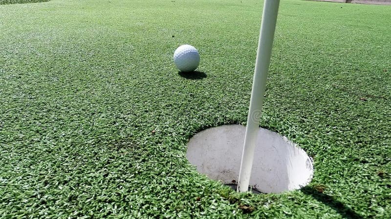 White golf ball hitting flag stick and falling into hole on putting green