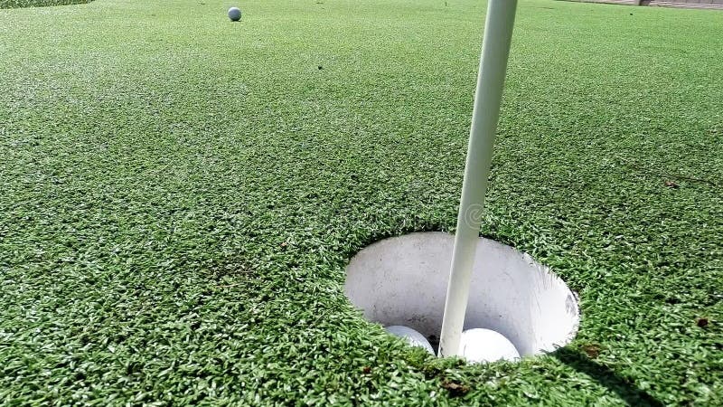 White golf ball hitting flag stick and falling into hole on putting green