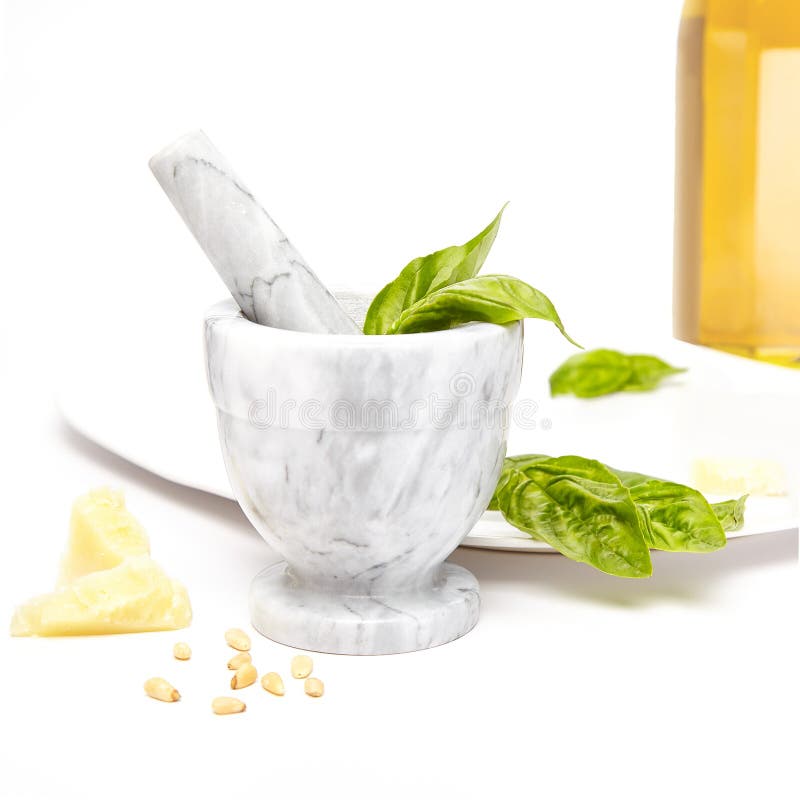 White and gray marble mortar and pestle with pesto ingredients, olive oil, basil, pine nuts, and parmesan cheese.