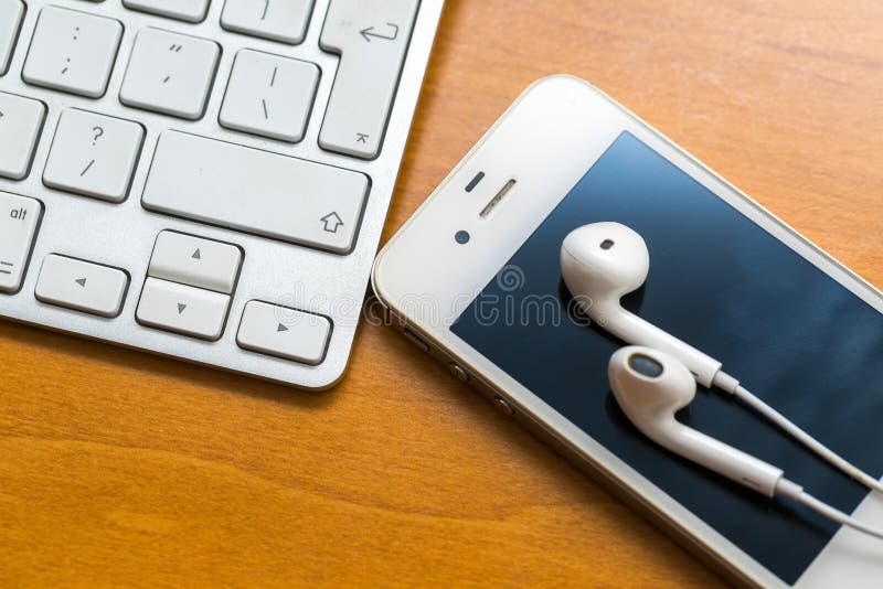 White headphones, cellphone and keyboard lying on wooden table stock photo