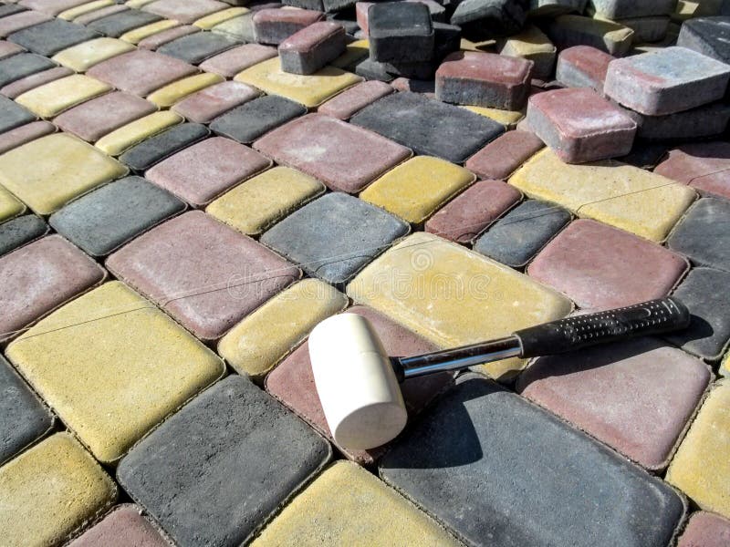 A white mallet, a building rope and a pile of bricks of sidewalk tiles against the background of newly laid paving slabs royalty free stock images