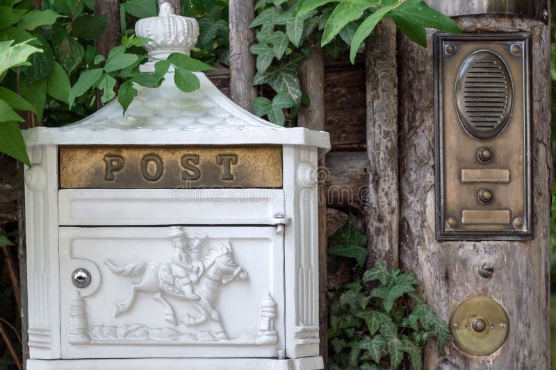 A White Metal Letter Box with Decorative Elements Hangs on the Fence