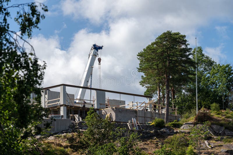 White Mobile Crane Towering Over a House on a Hill Under Construction