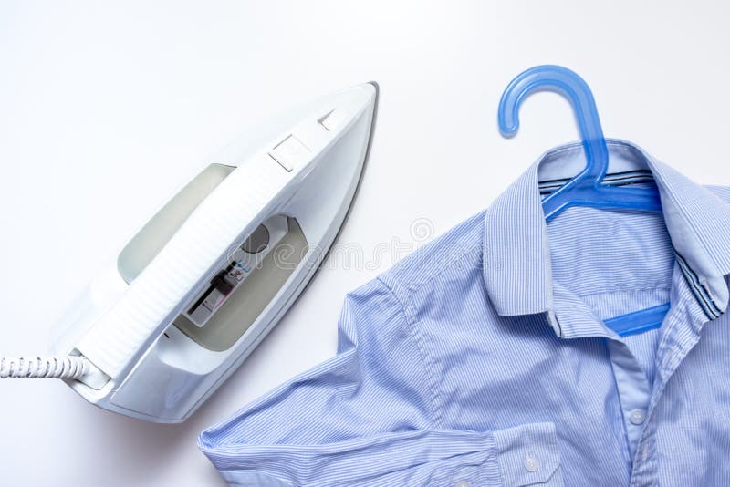 White modern electrical iron close up and blue shirts on the table, top view - ironing, laundry and housework concept stock photo