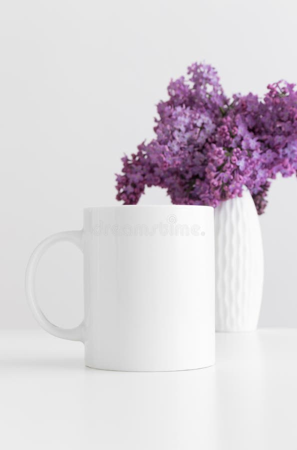 White mug mockup with a bouquet of lilac in a vase on a white table