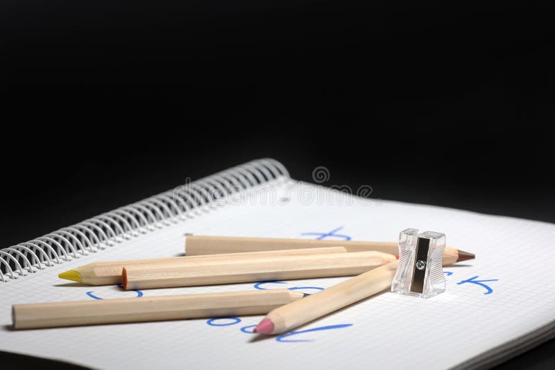 White notebook , color pencils and pencil sharpener on a table against black background. Preparing for a school.