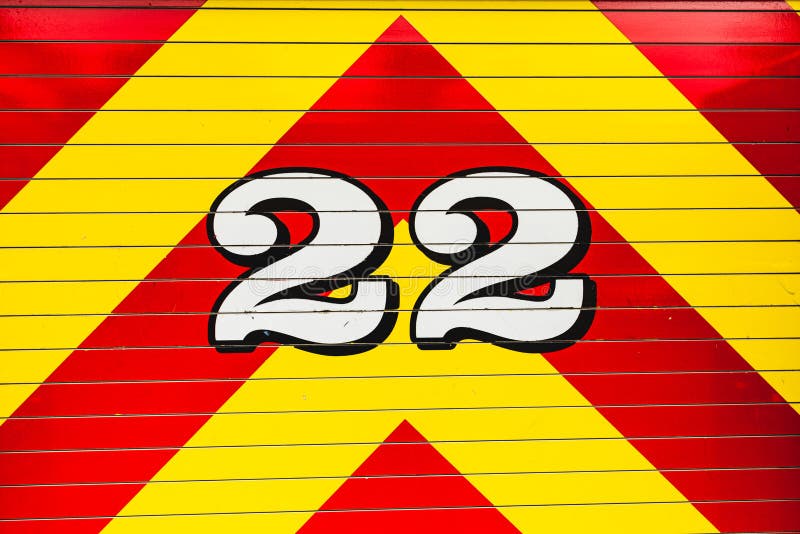 White number 22 outlined in black overlapping a bright red and bright yellow chevron pattern painted on fire truck. White number 22 outlined in black overlapping a bright red and bright yellow chevron pattern painted on fire truck