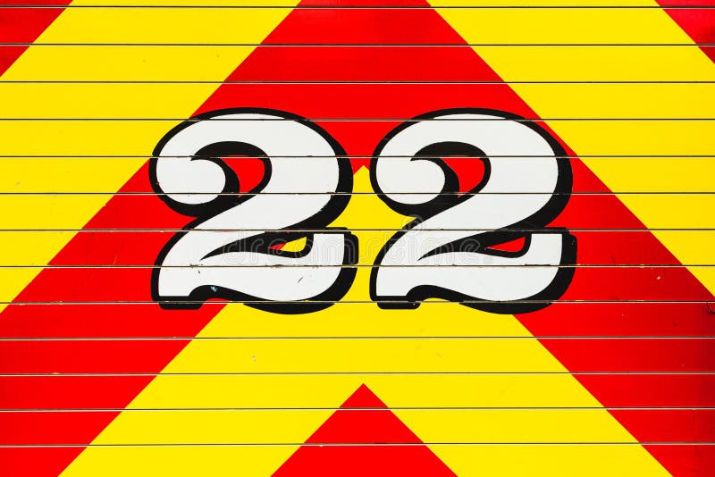 White number 22 outlined in black overlapping a bright red and bright yellow chevron pattern painted on fire truck. White number 22 outlined in black overlapping a bright red and bright yellow chevron pattern painted on fire truck