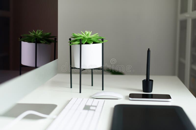 White office desk table with computer keyboard, mouse, monitor, graphic tablet, smartphone, succulent plant and other office