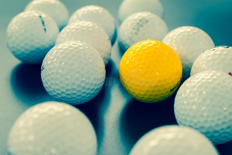 White and One Yellow Golf Balls on Black Floor. Individuality an Stock