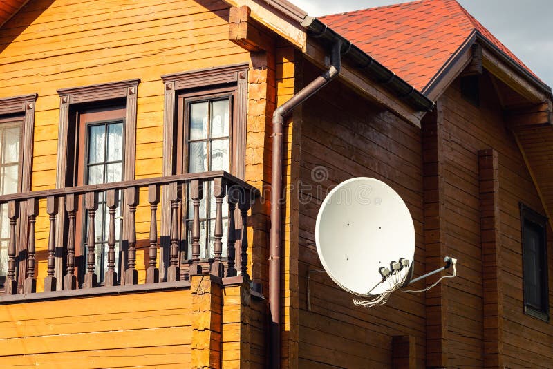 White parabolic satellite antena dish hanged on wall of modern wooden country house villa. Wireless television broadcasting reciever, technology, antenna, tv, home, roof, sky, communication, building, receiver, signal, radio, cable, architecture, outdoor, internet, aerial, information, telecommunication, wave, reception, digital, equipment, media, rural, network, transmit, channel, connection, data, space, global, telecast, metal, expensive, faraway, news