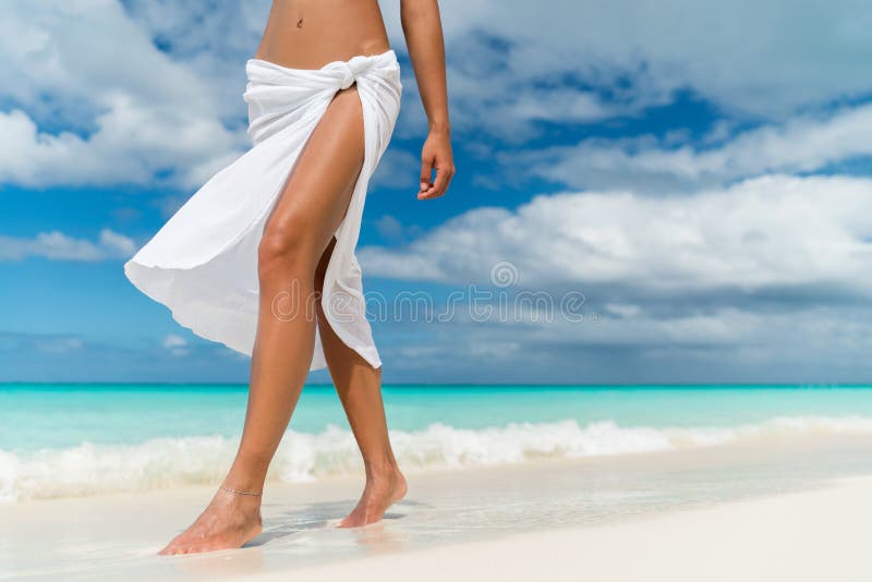 White pareo woman legs walking on tropical beach vacation