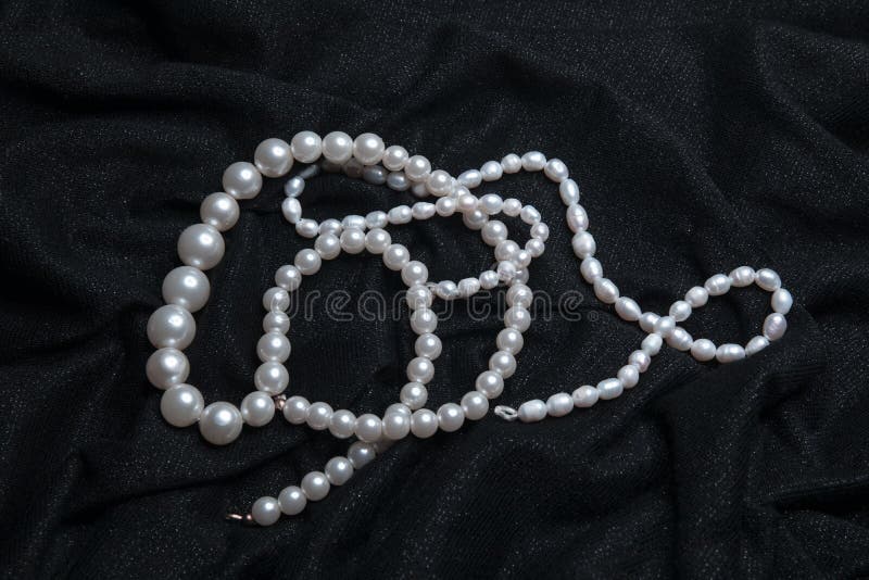 White pearls on the black shiny fabric background royalty free stock photography