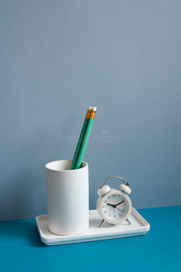 White Pencil Holder and Alarm Clock on Blue Desk. Workspace Office