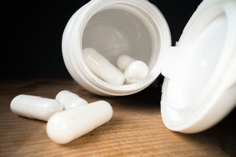 White pills or capsules next to bottle on wooden table background. Drug prescription, treatment medication. Pharmaceutical