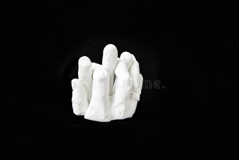 White plaster sculpture of intertwined fingers on a black background. High quality photo