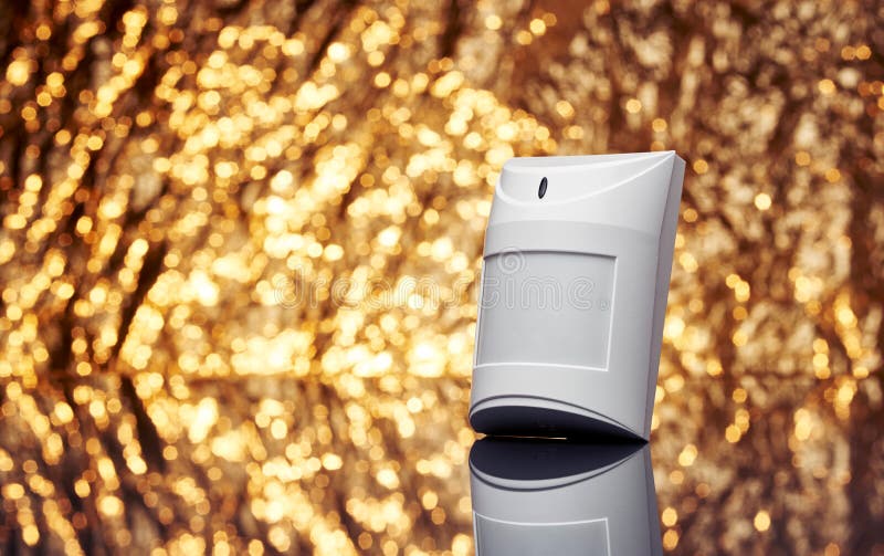 White plastic alarm motion sensor with fancy shiny gold background full of sparks out of focus.