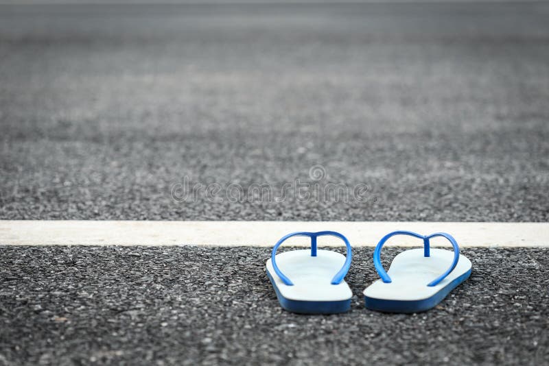 White plastic flip flop shoe on black asphalt road