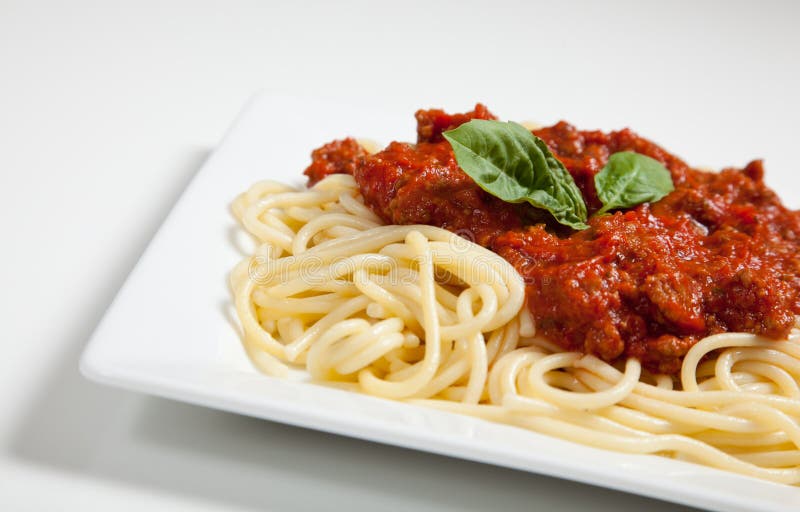 White plate of spaghetti and meat sauce with basil
