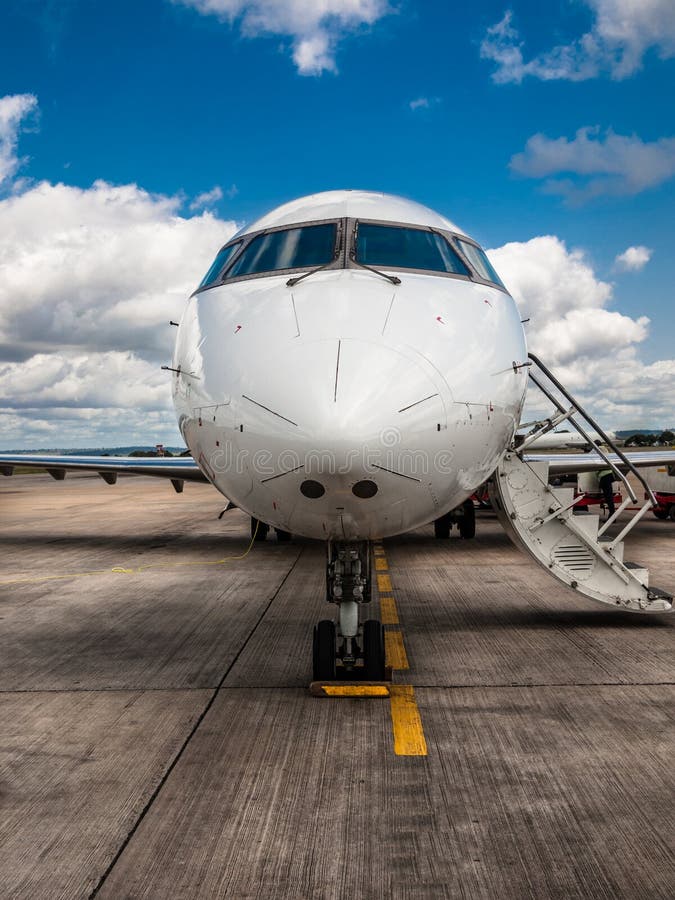 White private airplane closeup with folding ladder standing on the aerodrome field on a background of blue sky