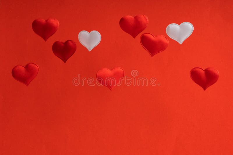 2 white and 7 red flying small textile hearts are on a background of red velvet paper