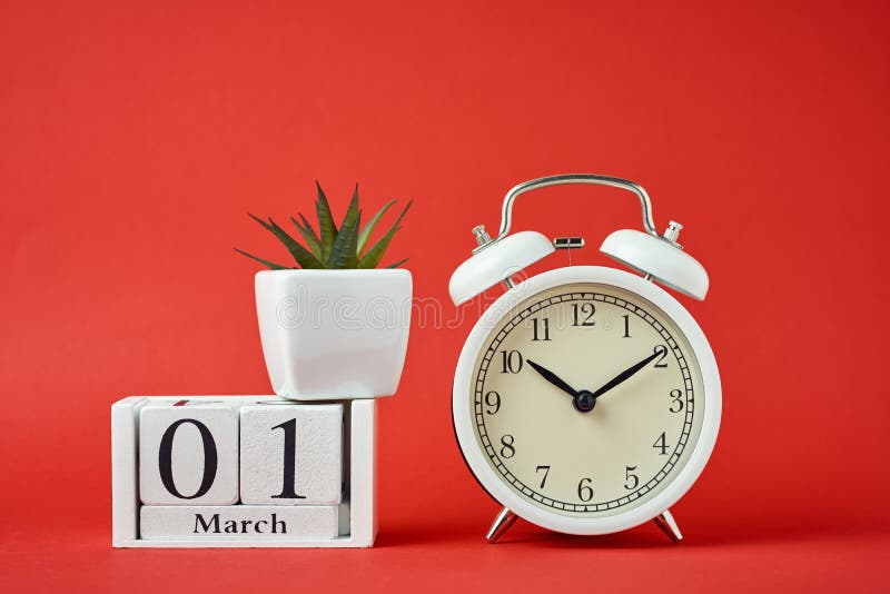 White retro alarm clock on red background and wooden calendar blocks with date 1 march on the red background. Time concept