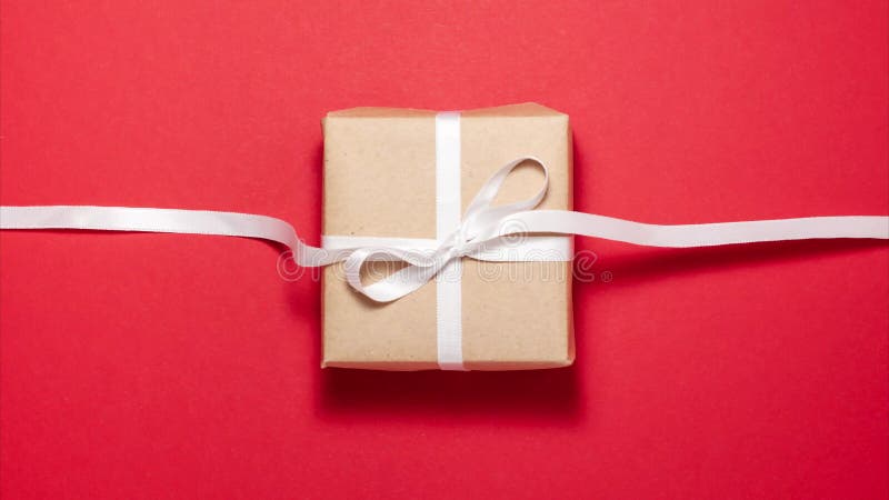 White ribbon tied in a gift bow on brown paper gift box on red background. Flat lay top view stop motion animation