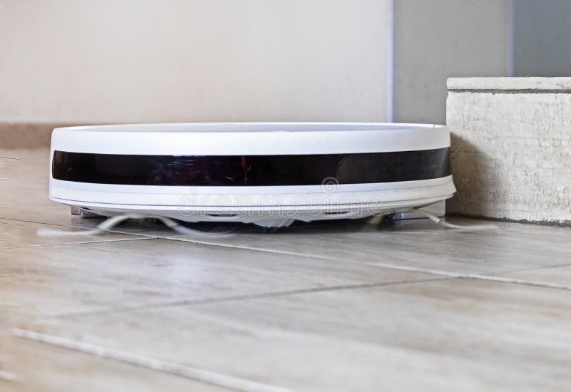White Robot Vacuum Cleaner Performs Automatic Cleaning in the Corner of
