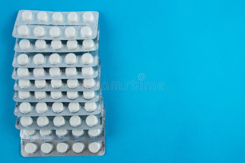 White Round Pills in Pack. Tablets are Next To the Packaging on a Blue