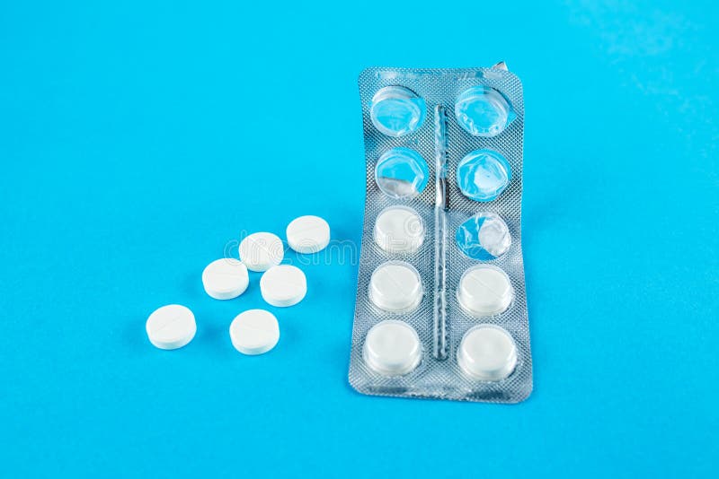 White Round Pills in Pack. Tablets are Next To the Packaging on a Blue