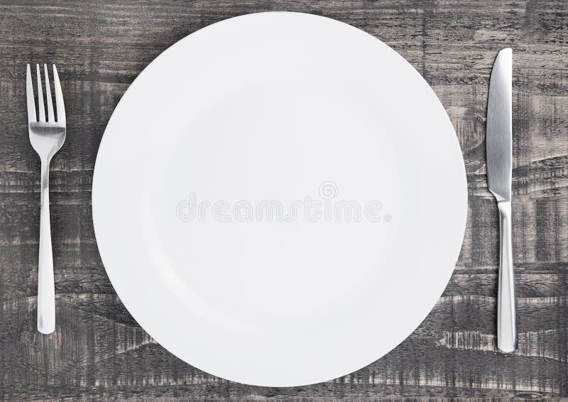 White round plate with fork and knife on wood. Copyspace, background.