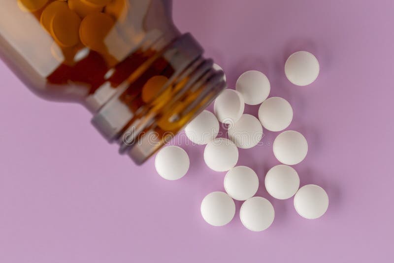 White round tablets scattered near glass bottle of pills