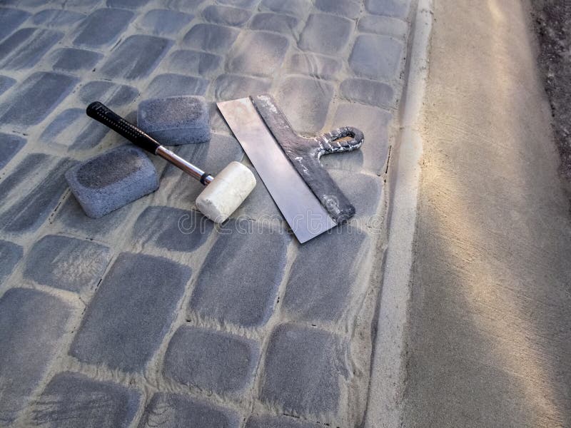 White rubber mallet and a large construction spatula lie on the surface of a newly laid gray paving slab with a concrete edge. stock photos