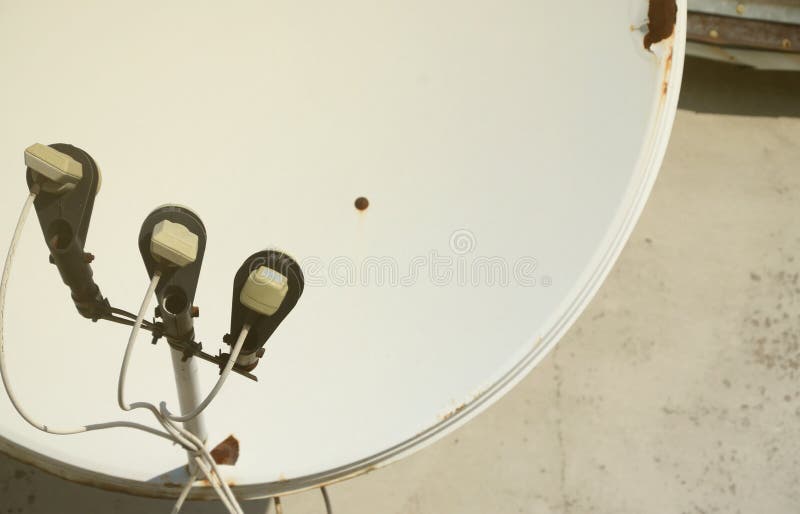White satellite dish with three converters mounted on residental building rooftop concrete wall. Satellite television advertisement