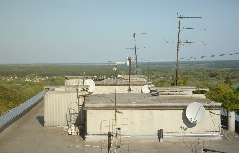 White satellite dish with three converters mounted on residental building rooftop concrete wall. Satellite television advertisement