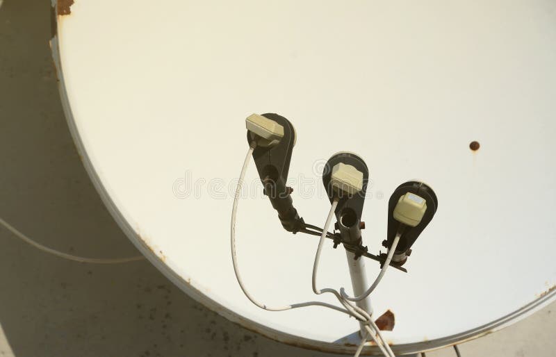 White satellite dish with three converters mounted on residental building rooftop concrete wall. Satellite television advertisement